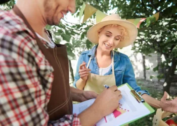 Agricultores analisam documentos e discutem gestão rural em feira ao ar livre, cercados por árvores.