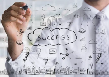 Homem com vestimenta formal escreve alguns símbolos em uma lousa transparente. Em destaque, a palavra "success", representando hábitos de pessoas milionárias.