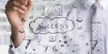 Rotina milionária: 5 hábitos das pessoas de sucesso 3 Homem com vestimenta formal escreve alguns símbolos em uma lousa transparente. Em destaque, a palavra "success", representando hábitos de pessoas milionárias.