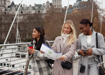 Três mulheres exploram uma cidade, planejando um intercâmbio de férias com mapa e celular.