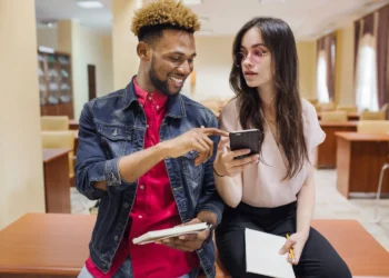 Dois jovens em ambiente acadêmico olhando para celular, representando cartões de crédito sem anuidade.