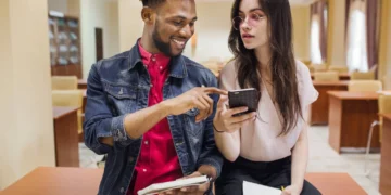 Dois jovens em ambiente acadêmico olhando para celular, representando cartões de crédito sem anuidade.