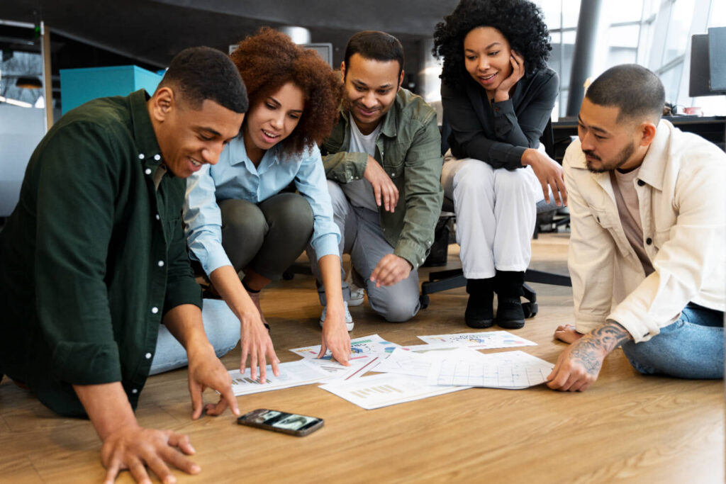 Grupo diverso analisando gráficos no chão, discutindo estratégias para negócios lucrativos em 2025.