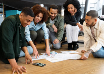 Grupo diverso analisando gráficos no chão, discutindo estratégias para negócios lucrativos em 2025.