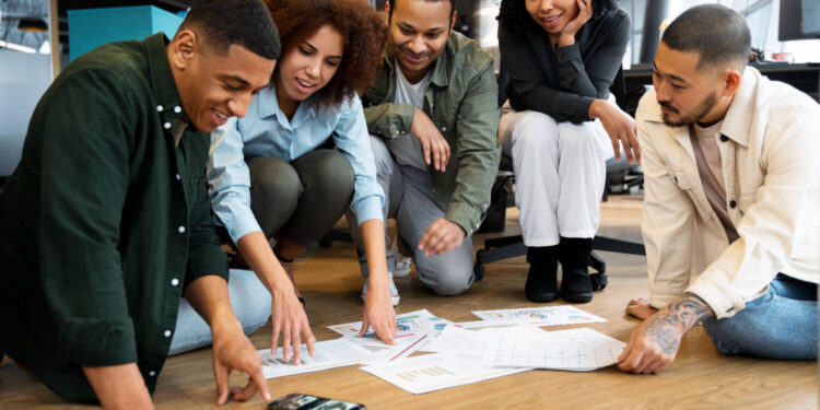 Grupo diverso analisando gráficos no chão, discutindo estratégias para negócios lucrativos em 2025.
