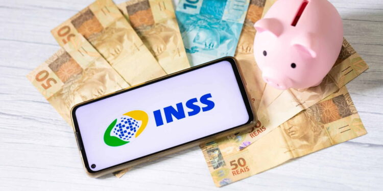 INSS divulga datas de pagamento de março; confira o calendário completo 14 Celular com símbolo do INSS na tela sobre notas de real espalhadas. Há um cofre em formato de porquinho na imagem, representando pagamento do INSS.