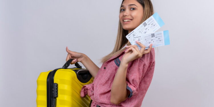 Passagens aéreas baratas: dicas infalíveis para economizar 16 Mulher sorridente exibe bilhetes de passagens aéreas enquanto segura uma mala de viagem amarela, representando passagens aéreas baratas.