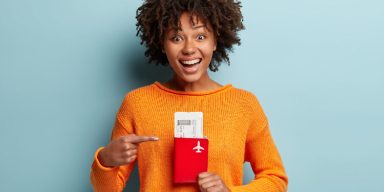Mulher sorridente segura e aponta para passaporte junto com passagem aérea.