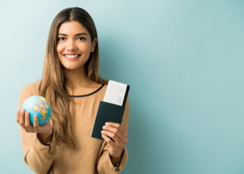 Mulher exibe um dos passaportes mais valiosos do mundo em uma das mãos e segura um pequeno mapa em forma de globo Terra na outra mão.