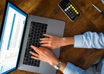 Pessoa responde a pesquisas pagas em seu notebook. Próximo a ele há um celular com uma calculadora aberta.