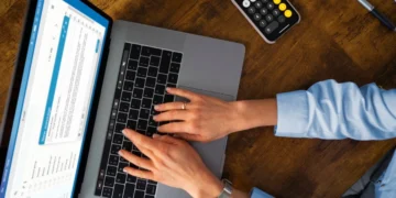 Ganhe dinheiro sem sair de casa: 3 plataformas de pesquisas pagas para você começar hoje 3 Pessoa responde a pesquisas pagas em seu notebook. Próximo a ele há um celular com uma calculadora aberta.