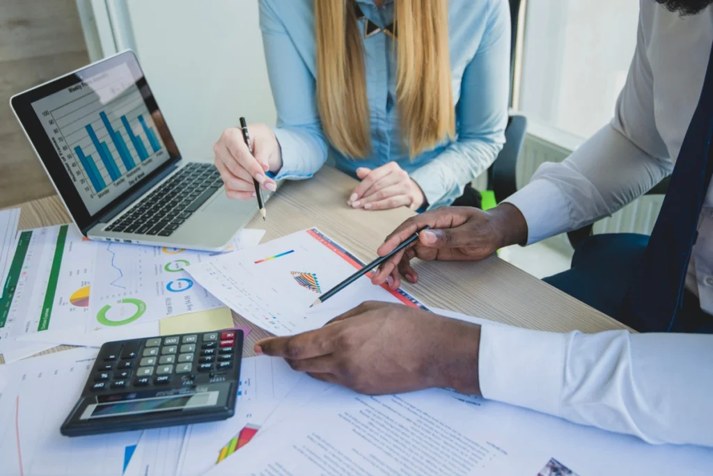 Dois profissionais analisam documentos e gráficos em meio a um planejamento fiscal.