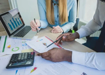 Dois profissionais analisam documentos e gráficos em meio a um planejamento fiscal.