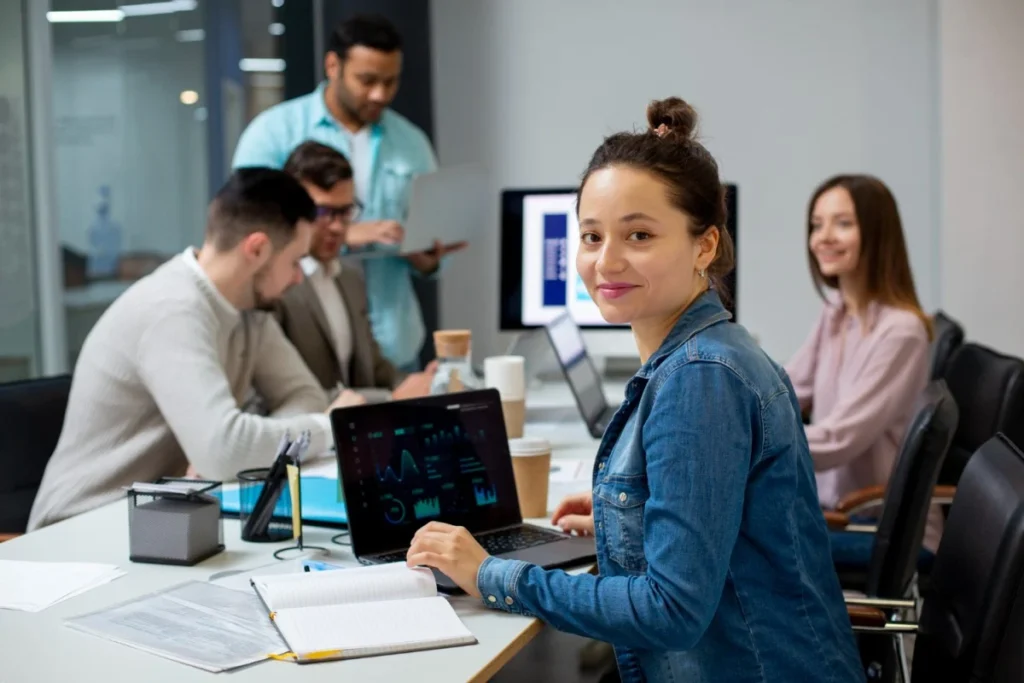 Profissionais se reúnem em sala de trabalho, cada um com seu computador. Representando profissões em alta em 2025.