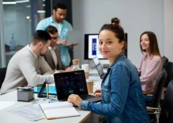 Profissionais se reúnem em sala de trabalho, cada um com seu computador. Representando profissões em alta em 2025.