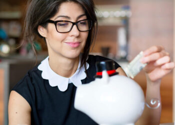 Mulher sorridente colocando dinheiro em um cofrinho, simbolizando renda extra nos finais de semana.
