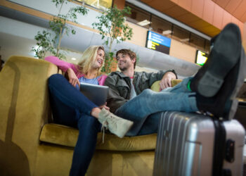 Casal sorridente relaxa em poltrona com mala em salas VIP do aeroporto, aguardando o voo.