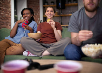 Grupo de amigos assistindo a séries em alta na Netflix em 2025, sorrindo no sofá com pipoca e snacks.