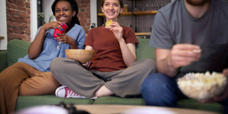 Grupo de amigos assistindo a séries em alta na Netflix em 2025, sorrindo no sofá com pipoca e snacks.