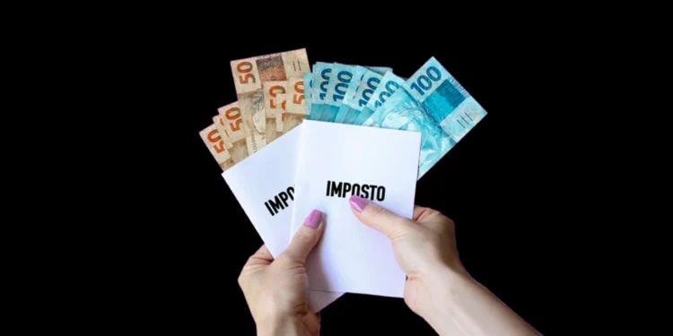 Tributação no Brasil: entenda as regras atuais 14 Mãos de uma mulher segura notas de R$ 50 e R$ 100 e dois folhetos onde está escrito "imposto". Falando sobre a tributação no Brasil.
