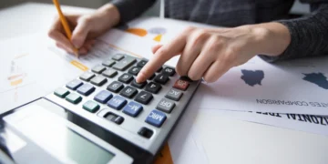 Tributos municipais, estaduais e federais: qual a diferença? 1 Homem usa calculadora e faz algumas anotações para medir tributos devidos.