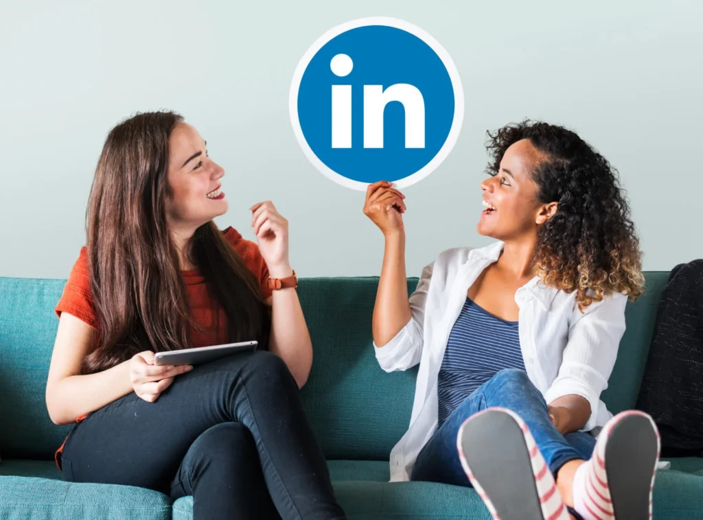 Duas mulheres sorrindo em um sofá, segurando o logo do LinkedIn e discutindo LinkedIn para negócios.