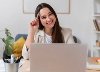 Mulher sorri e aponta caneta para a cabeça enquanto faz busca por vagas de emprego online.