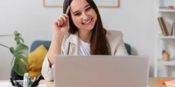 Vagas de emprego online: onde encontrar e como se candidatar 5 Mulher sorri e aponta caneta para a cabeça enquanto faz busca por vagas de emprego online.