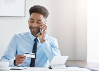Homem em uma mesa segurando um cartão ao telefone, representando bancos brasileiros na lista da Forbes.