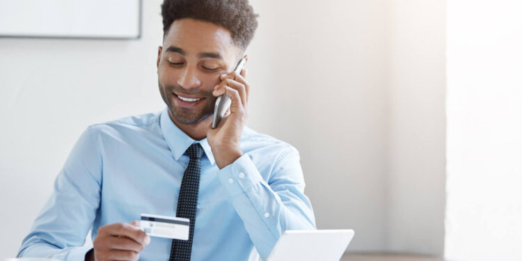 Homem em uma mesa segurando um cartão ao telefone, representando bancos brasileiros na lista da Forbes.