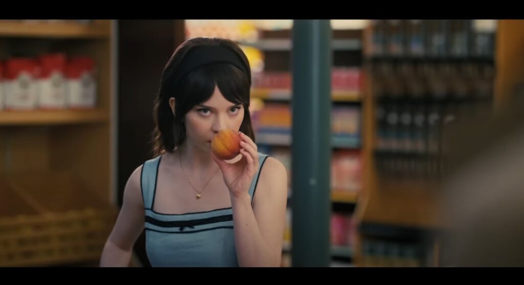 Filmes de suspense psicológico: Mulher de vestido azul cheira um pêssego no mercado, olhando pensativa.
