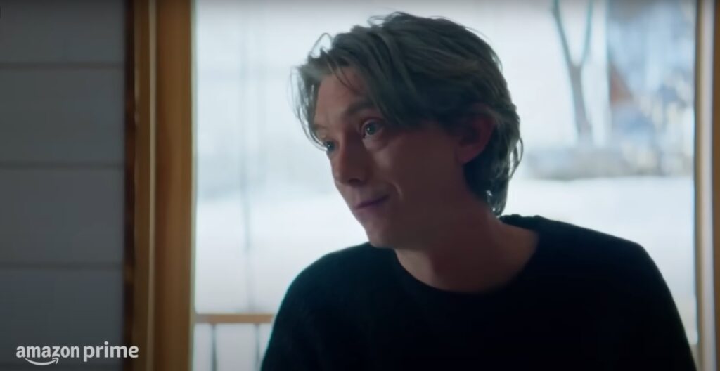 Filmes de suspense psicológico: Homem jovem de cabelos grisalhos sorri enigmaticamente em um ambiente iluminado.