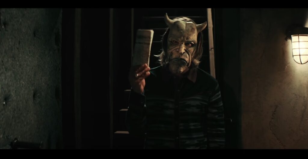 Filmes de suspense psicológico: Homem mascarado com chifres segura um jornal em uma sala escura e assustadora.