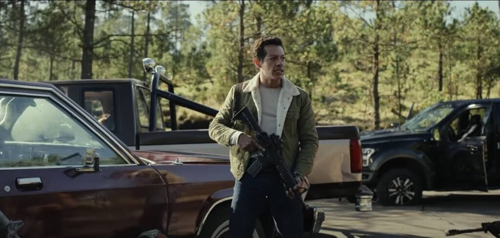 Confira os 5 Melhores Filmes de Ação para Assistir na Netflix em 2025 22 Homem armado em cena intensa de um dos melhores filmes de ação, cercado por veículos danificados.