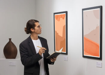 Homem anotando detalhes de pinturas abstratas, demonstrando como escolher obras de arte com atenção.