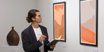 Homem anotando detalhes de pinturas abstratas, demonstrando como escolher obras de arte com atenção.