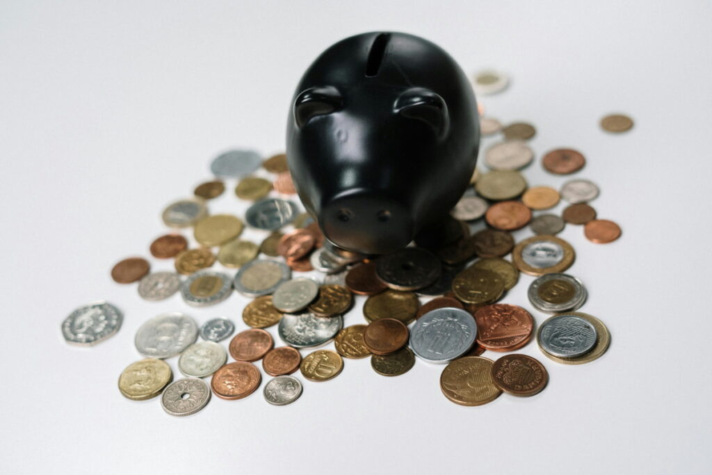 Cofre em formato de porquinho na cor preta, com algumas moedas em volta. Mostrando como juntar 10 mil em 1 ano.
