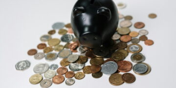 Cofre em formato de porquinho na cor preta, com algumas moedas em volta. Mostrando como juntar 10 mil em 1 ano.