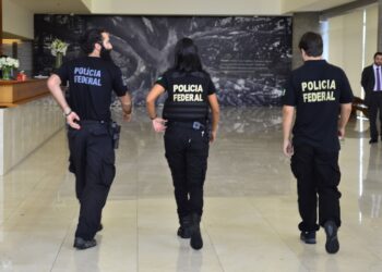 Três agentes da Polícia Federal caminham em saguão. Representando "concurso PF".
