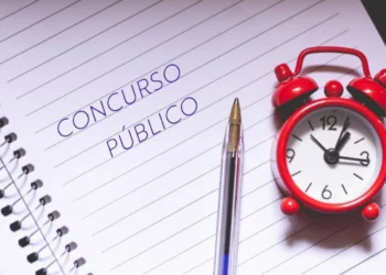 Folha de caderno onde está escrito "concurso público". Há também um despertador clássico na cor vermelha sobre essa folha. Falando sobre o concurso público da prefeitura de itatiba.