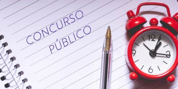 Folha de caderno onde está escrito "concurso público". Há também um despertador clássico na cor vermelha sobre essa folha. Falando sobre o concurso público da prefeitura de itatiba.