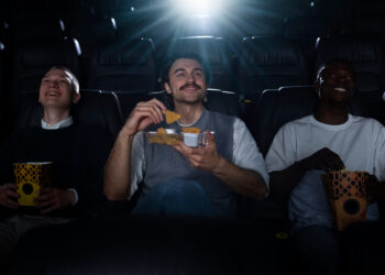 Três homens assistem e riem enquanto comem, curtindo filmes favoritos dos bilionários.