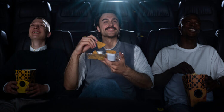 Três homens assistem e riem enquanto comem, curtindo filmes favoritos dos bilionários.