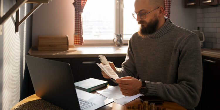 Homem sentado em mesa com laptop e documentos, analisando finanças para MEI.