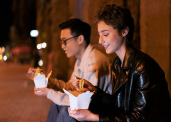 Dois jovens apreciando comida de rua à noite, refletindo hábitos culturais da classe alta.