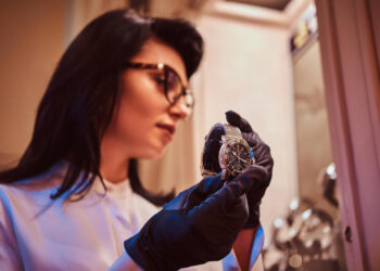 Mulher examinando relógio de luxo com luvas, destacando hobbies de luxo.