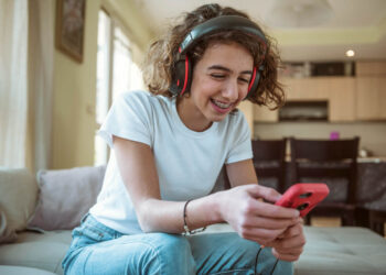 Uma mulher sorridente usando fones de ouvido enquanto joga em um celular, simbolizando jogos que pagam dinheiro.