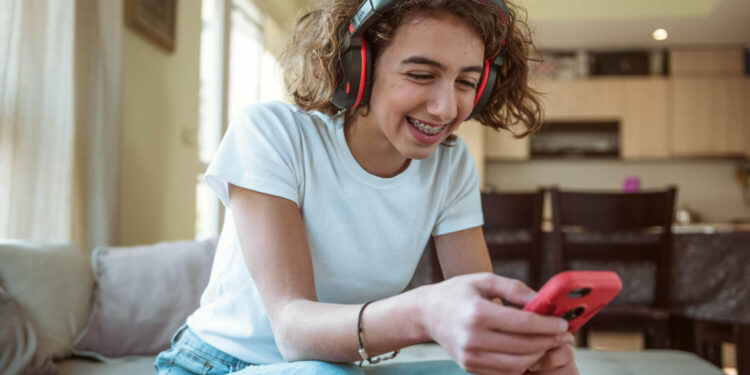 Uma mulher sorridente usando fones de ouvido enquanto joga em um celular, simbolizando jogos que pagam dinheiro.