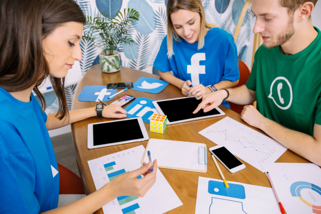 Equipe analisando dados e dispositivos, discutindo estratégias com prompts para criar conteúdos.