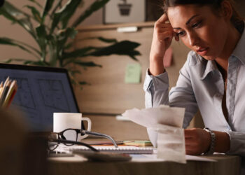 Mulher concentrada em documentos financeiros, destacando a necessidade de planejamento para uma reserva de emergência.